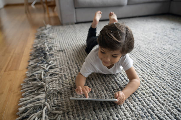 Smiling girl looking in tab laying on rug | H&R Carpets and Flooring